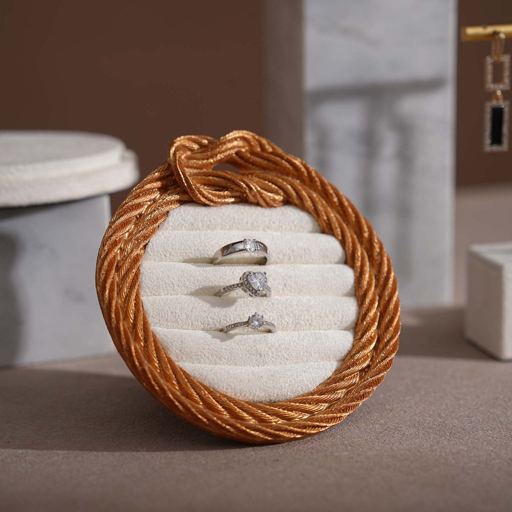 Round jewelry holder with rope design containing three rings on a neutral background
