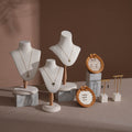 Jewelry display setup with necklaces on mannequin heads and earrings in woven holders against a brown background.