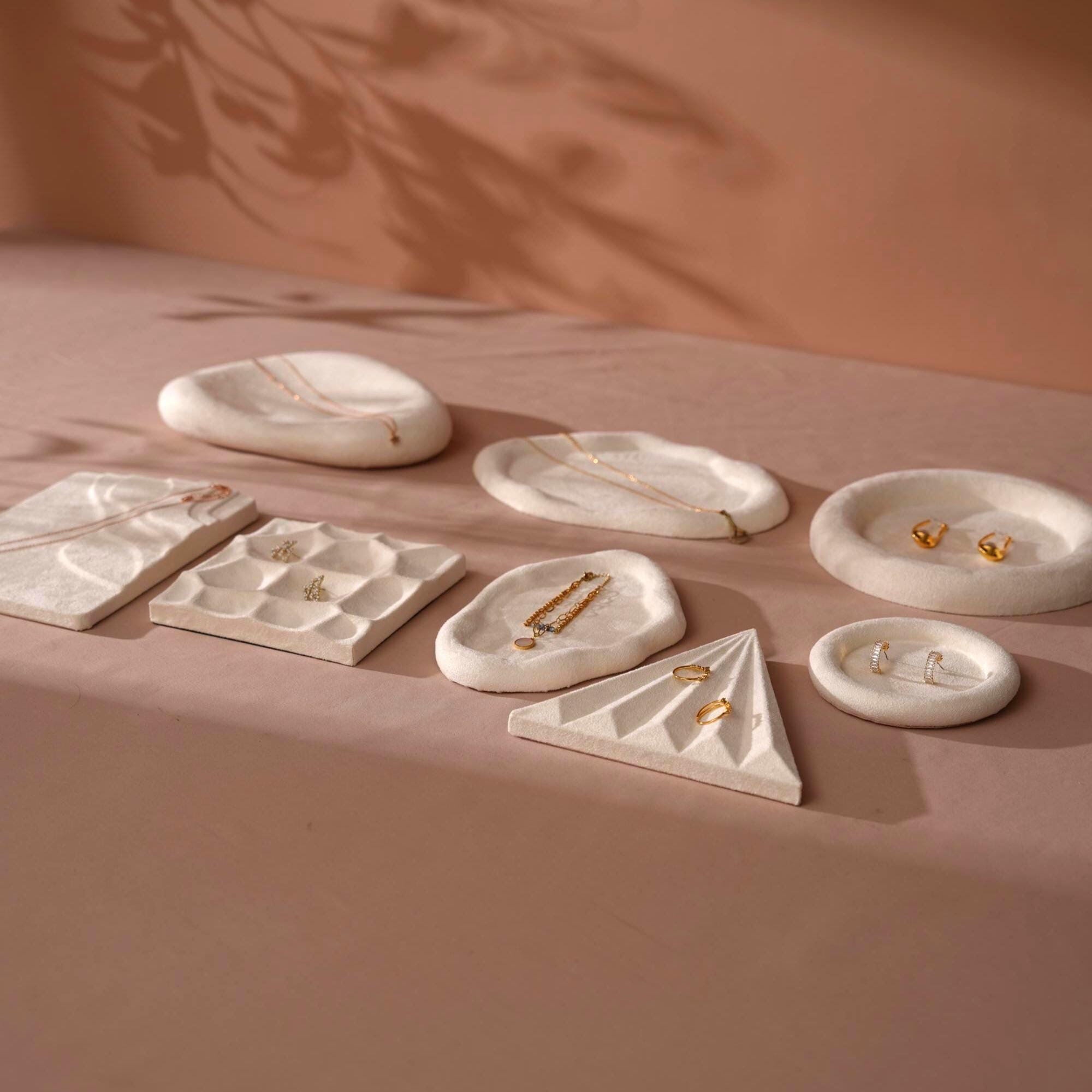 Cream white vegan suede jewelry display trays styled with earrings and chains on a warm background